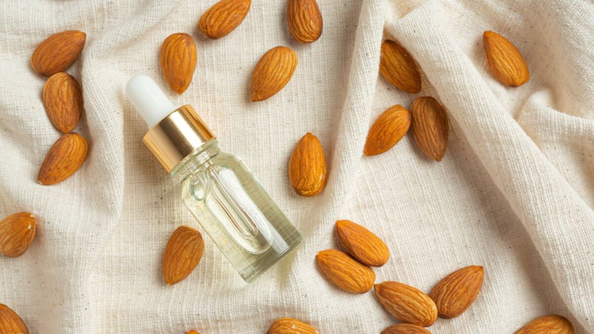 Butelka z olejem ze słodkich migdałów leżąca na lnianym materiale w otoczeniu migdałów